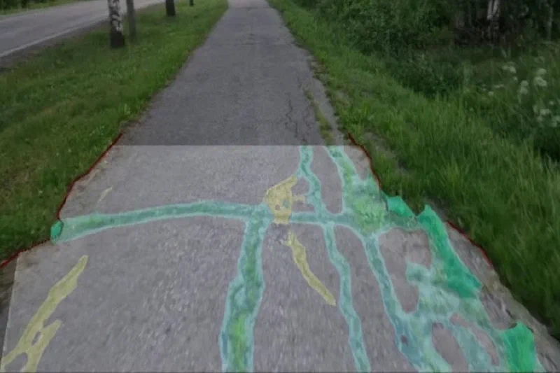 A cracked cycle path seen from a bicycle, with the cracks found by computer vision coloured over the pavement